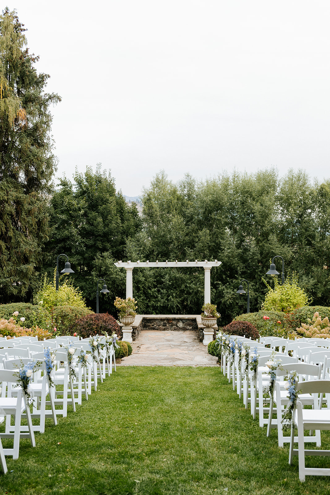 Ceremony chair rentals facing a stone pergola at a garden wedding in Eastern Washington