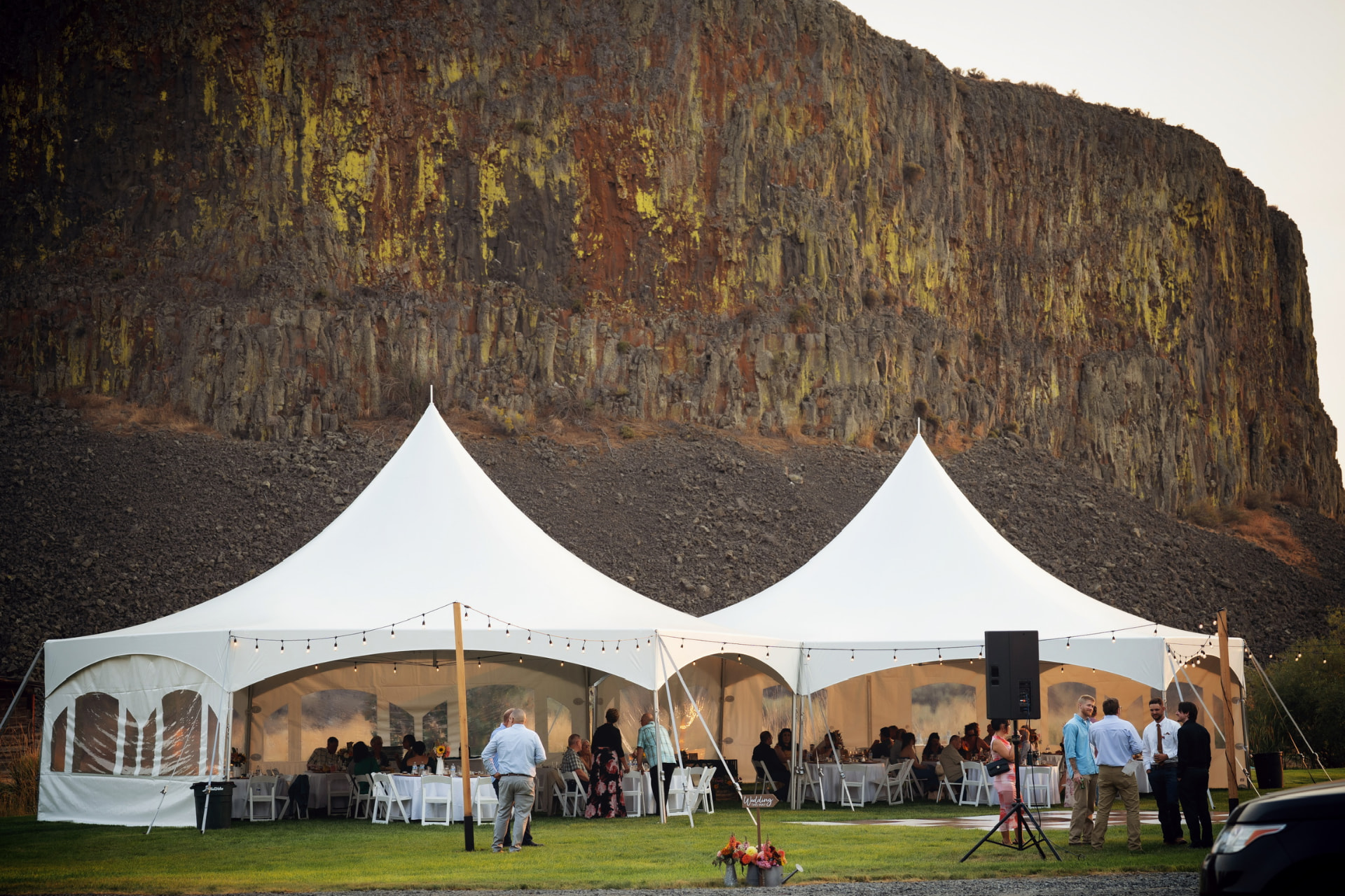 Wedding reception under a clear-top tent with farmhouse tables and string lights at sunset in Washington wine country